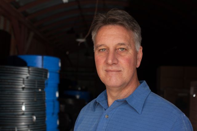 a man with grey hair in a blue striped polo looking in the camera