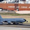 A U.S. airforce airplane taking of of a runway with a sign reading "Tinker Air Force Base" behind it on a brick building